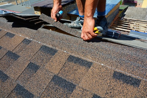 man installing new shingles on roof